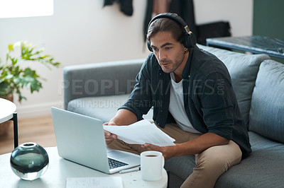 Buy stock photo Shot of a young man doing paperwork while using a laptop at home