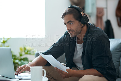 Buy stock photo Shot of a young man doing paperwork while using a laptop at home