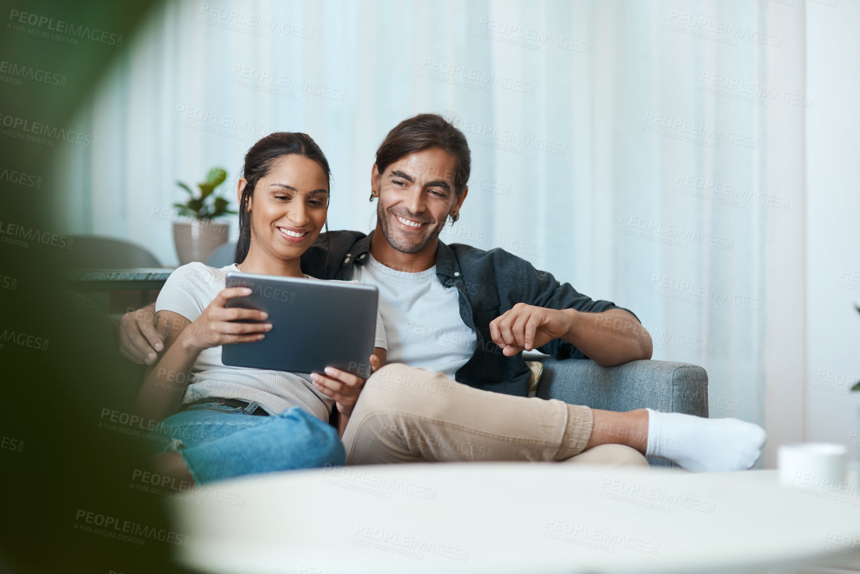 Buy stock photo Shot of a young couple sitting on a couch while using a digital tablet at home