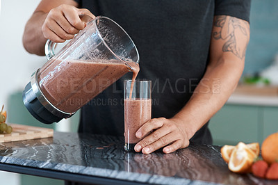 Buy stock photo Cropped shot of an unrecognizable young man making smoothies in his kitchen at home