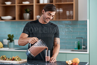 Buy stock photo Cropped shot of a handsome young man making smoothies in his kitchen at home
