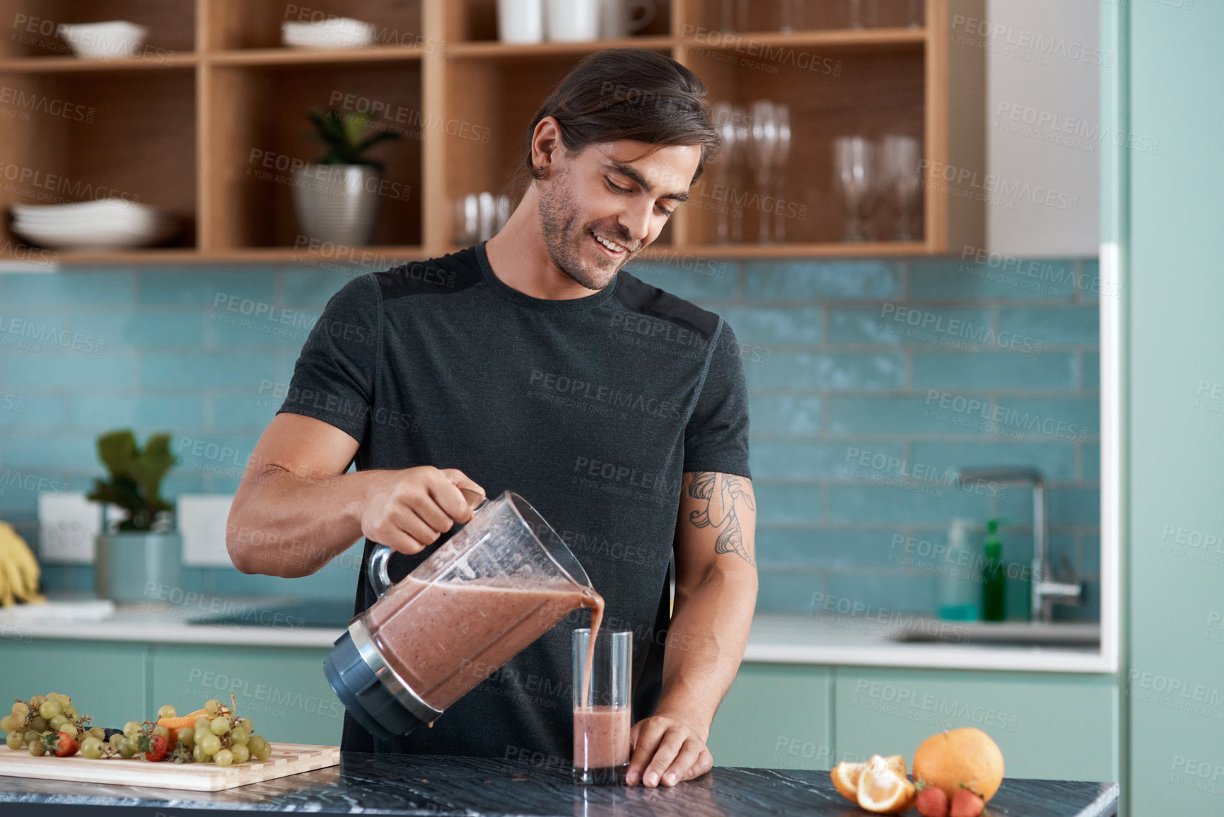 Buy stock photo Cropped shot of a handsome young man making smoothies in his kitchen at home