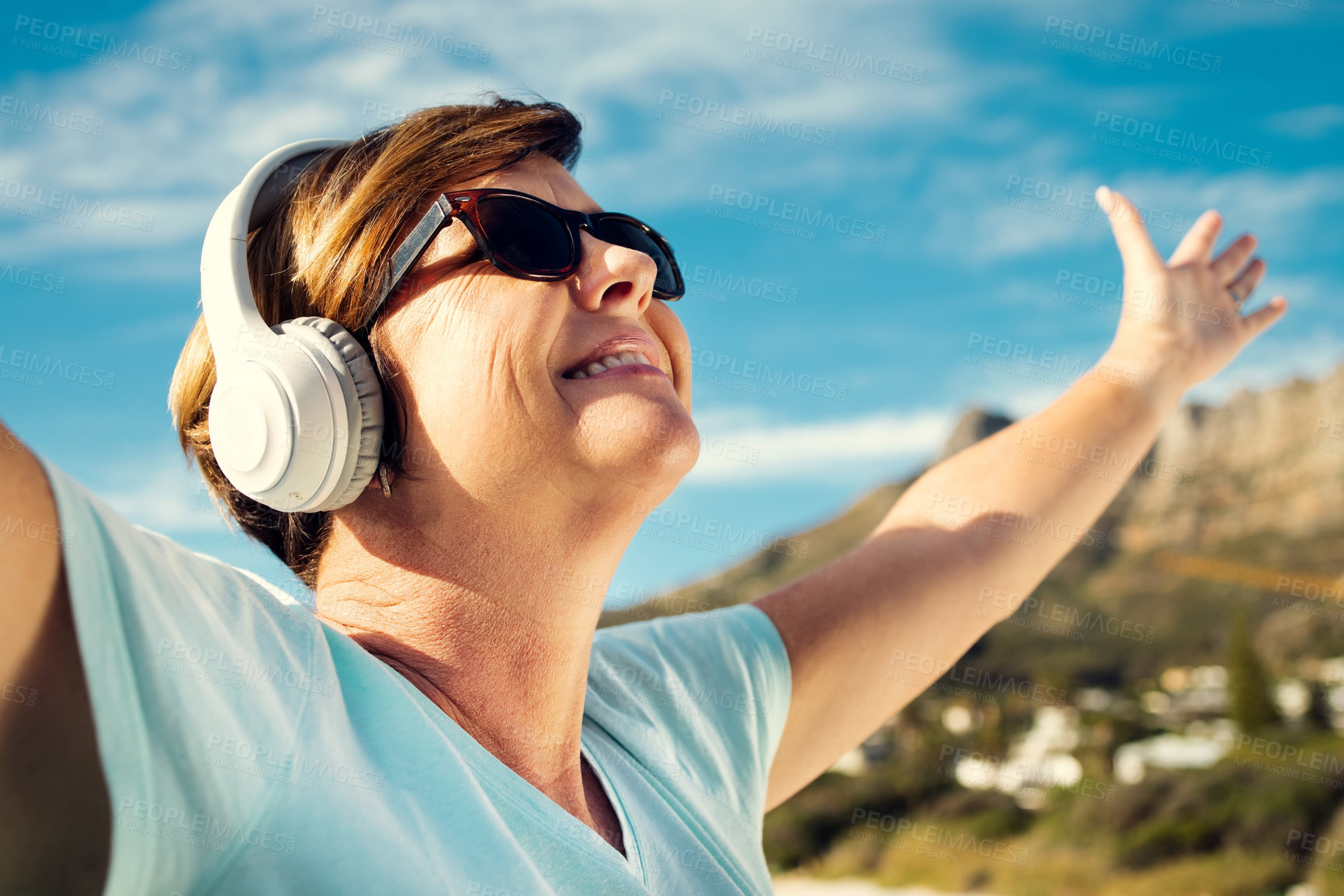 Buy stock photo Shot of a woman wearing headphones while standing outdoors