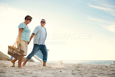 Buy stock photo Shot of a couple out at the beach with a picnic basket and chairs