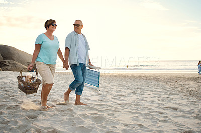 Buy stock photo Shot of a couple out at the beach with a picnic basket and chairs