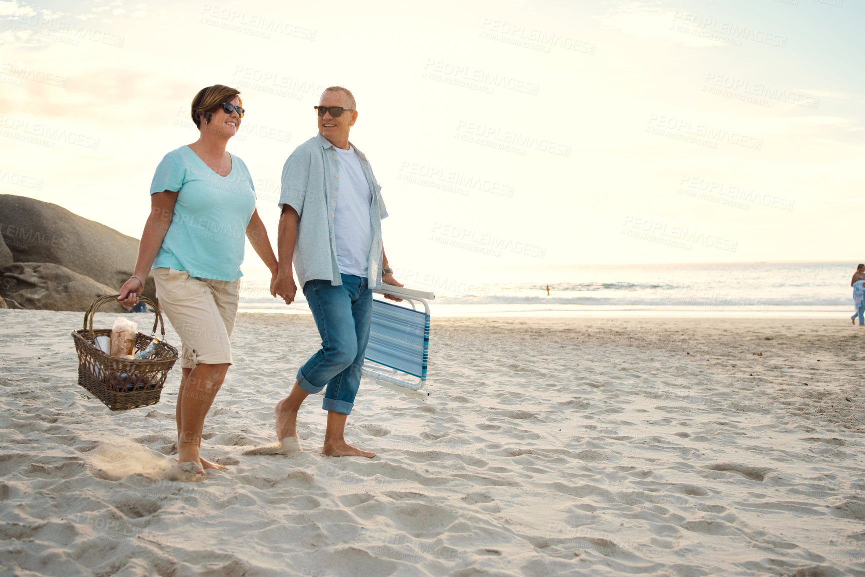 Buy stock photo Shot of a couple out at the beach with a picnic basket and chairs