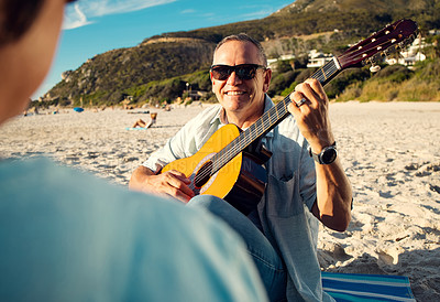 Buy stock photo Shot of a man playing the guitar while at the beach with his wife