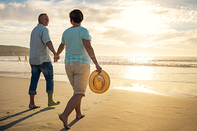 Buy stock photo Shot of a mature couple holding hands while walking on the beach