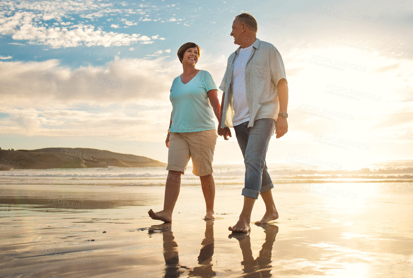 Buy stock photo Shot of a mature couple holding hands while walking on the beach