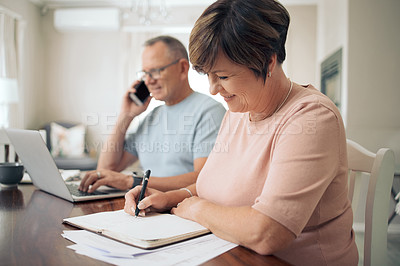 Buy stock photo Shot of a mature woman taking notes while her husband uses his smartphone