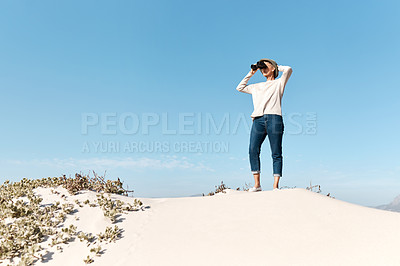 Buy stock photo Full length shot of an attractive mature woman using her binoculars while standing on the beach