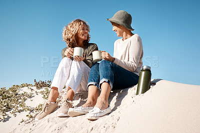 Buy stock photo Full length shot of two attractive mature women enjoying some coffee while sitting on the beach