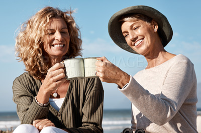 Buy stock photo Cropped shot of two attractive mature women enjoying some coffee while sitting on the beach