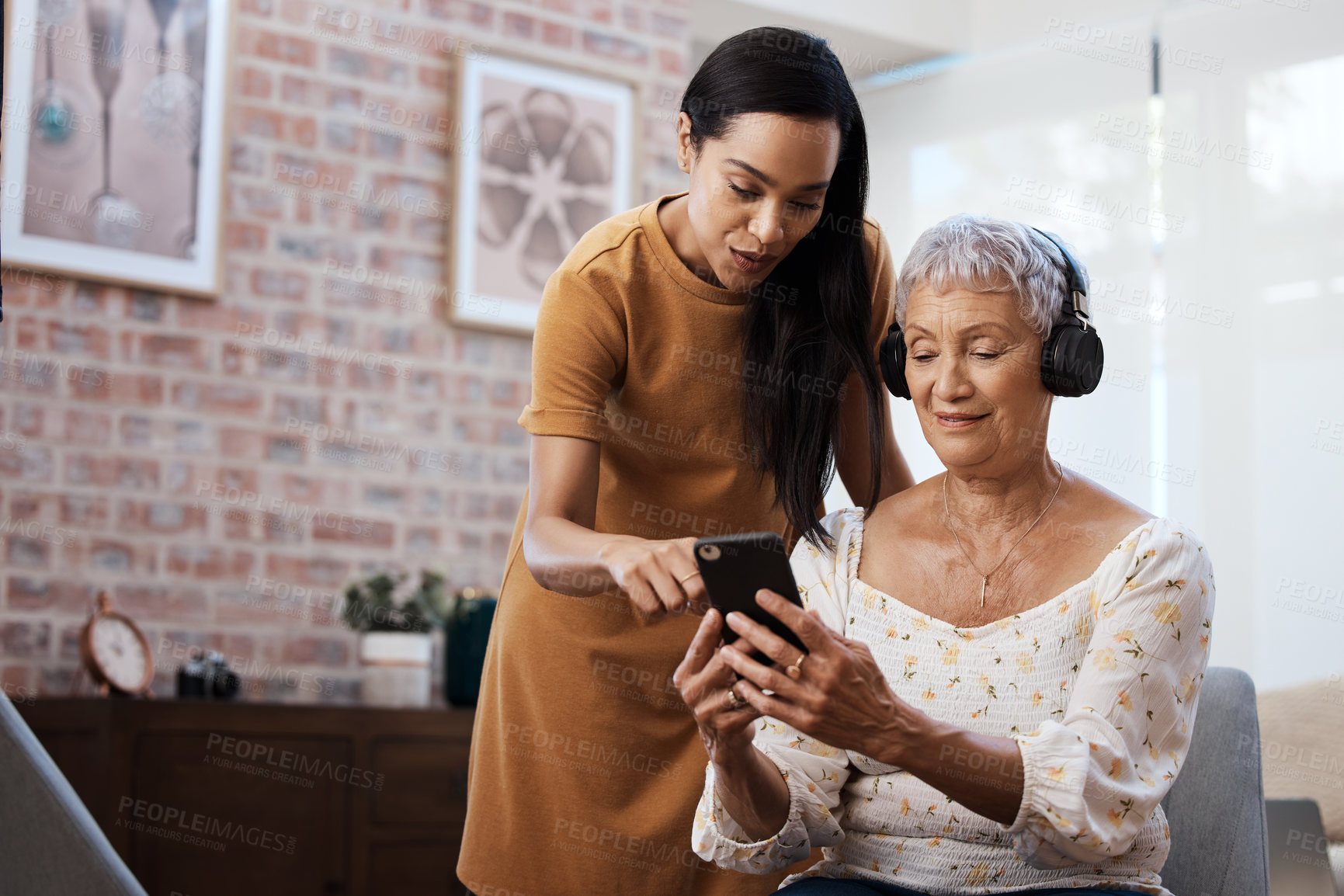 Buy stock photo Shot of a senior woman using a smartphone and headphones with her daughter at home