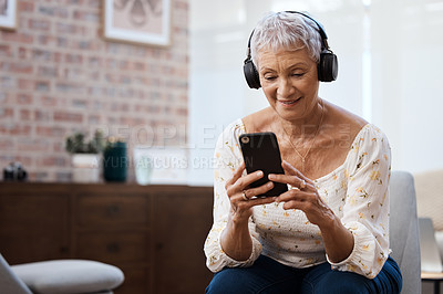 Buy stock photo Shot of a senior woman using a smartphone and headphones on the sofa at home