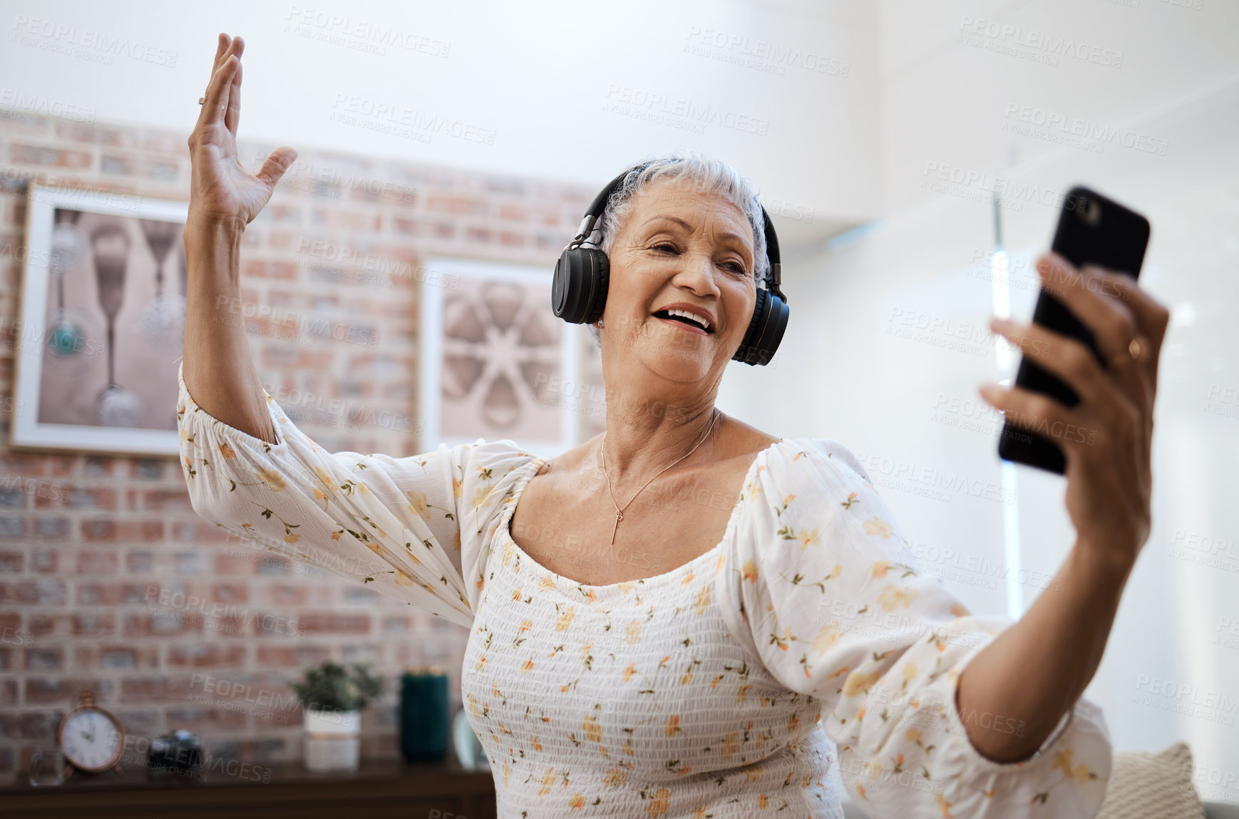 Buy stock photo Shot of a senior woman dancing while using a smartphone and headphones at home