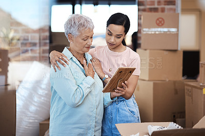 Buy stock photo Shot of a senior woman looking at a photograph with her daughter while packing boxes on moving day