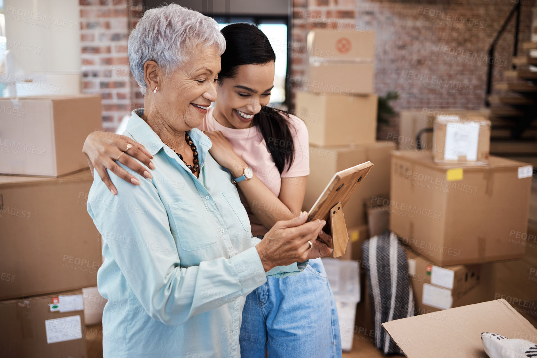 Buy stock photo Shot of a senior woman looking at a photograph with her daughter while packing boxes on moving day