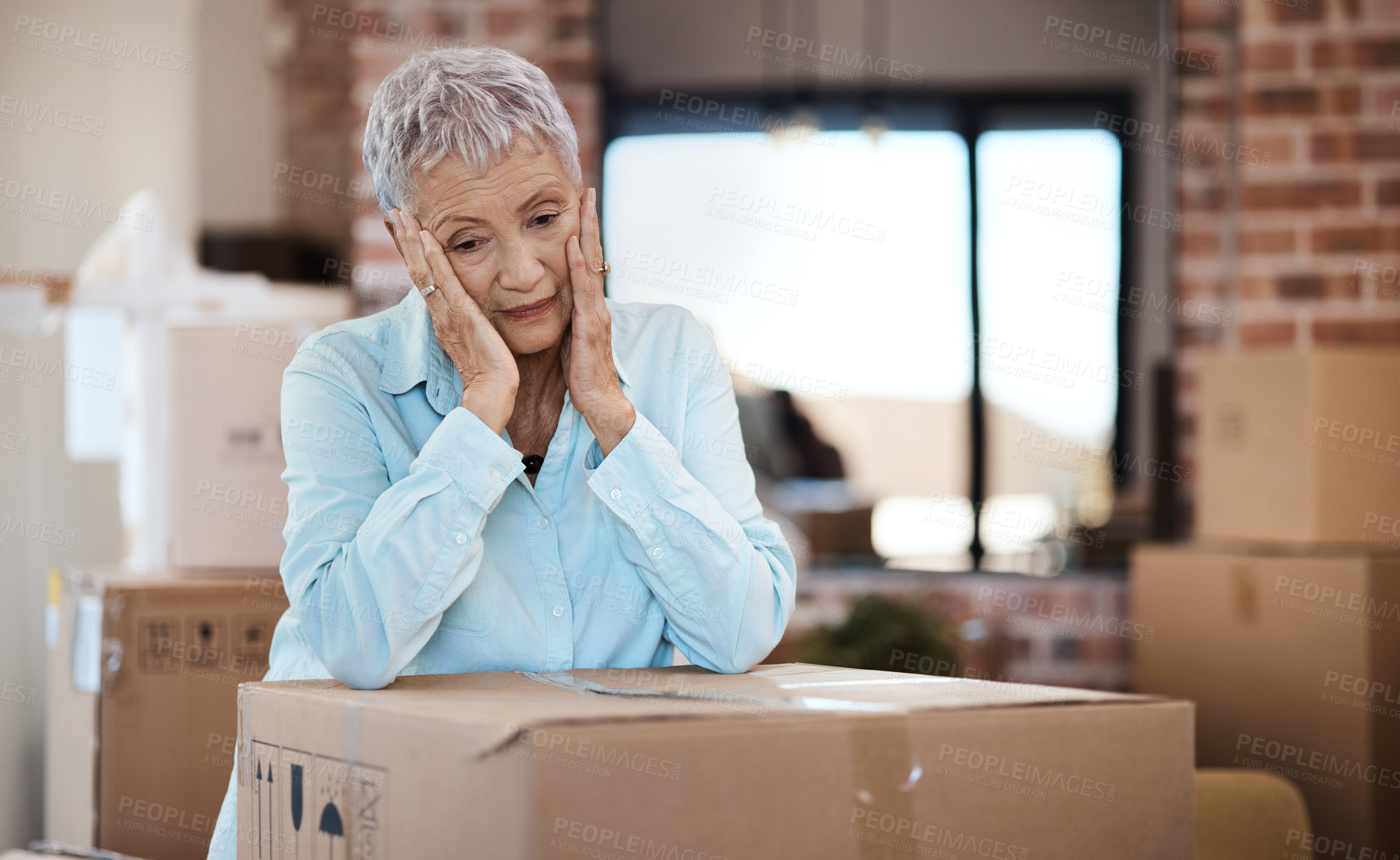 Buy stock photo Shot of a senior woman looking unhappy while moving house