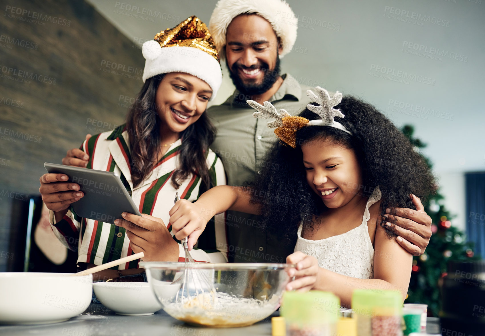 Buy stock photo Christmas, family and baking with a girl and parents mixing dough while using an online tablet recipe together. Food, children and kitchen with a mother, father and daughter learning to bake