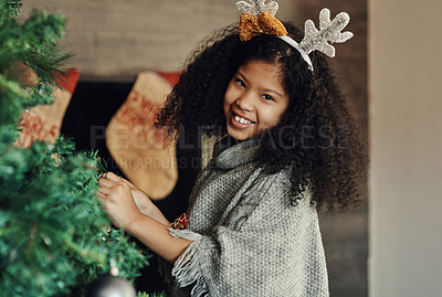 Buy stock photo Christmas, tree and decorating with a girl in antlers putting an ornament on a branch in the living room of her home. Children, portrait and smile with a happy kid placing decorations for celebration