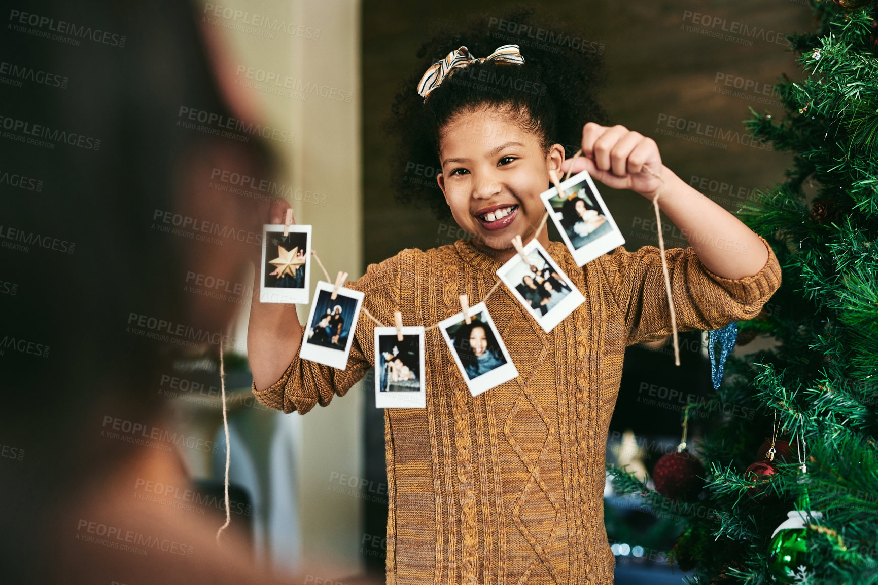 Buy stock photo Girl, photo string or hanging on christmas tree, family home or decoration in holiday happiness. Child, pictures or interior design for celebration, party or event in house with smile, art and tree