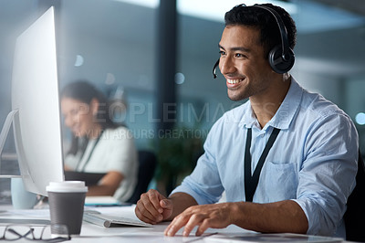 Buy stock photo Shot of a young man using a headset and computer in a modern office