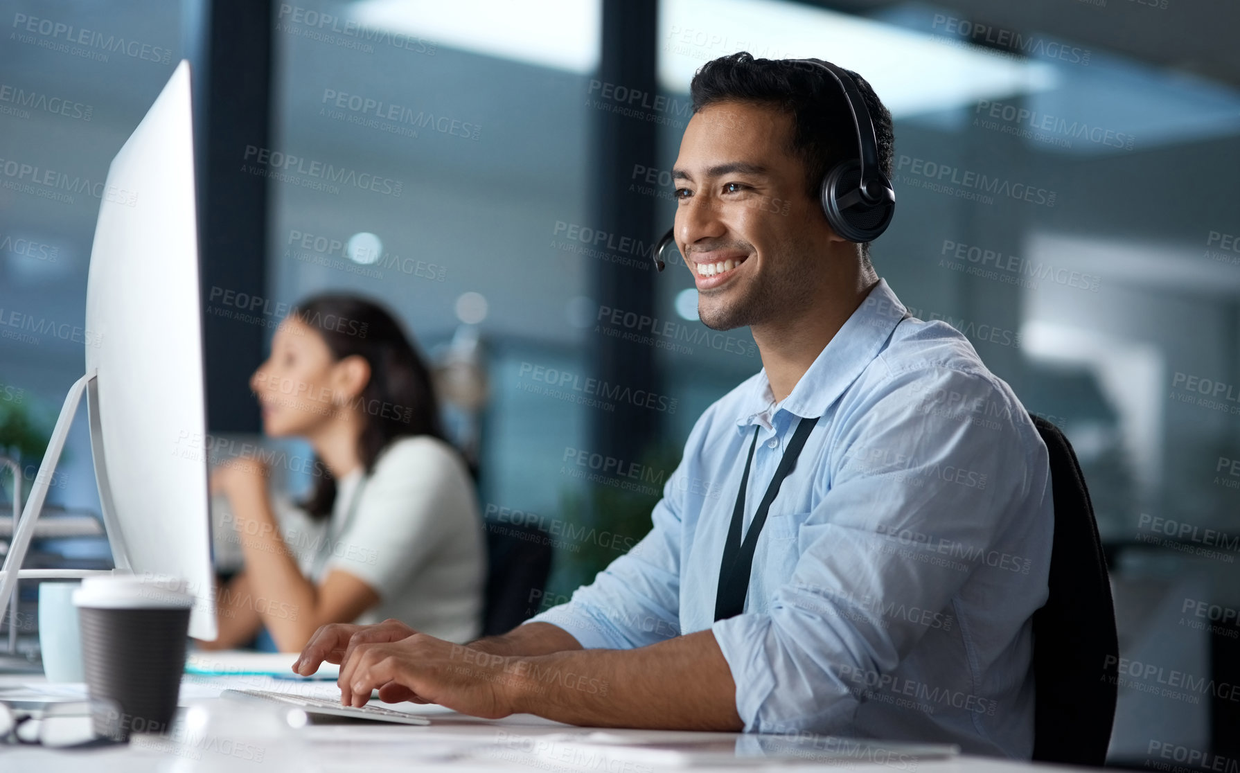 Buy stock photo Shot of a young man using a headset and computer in a modern office