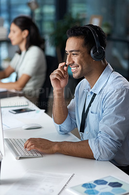 Buy stock photo Shot of a young man using a headset and computer in a modern office