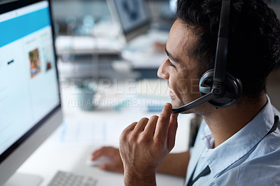 Buy stock photo Shot of a young man using a headset and computer in a modern office