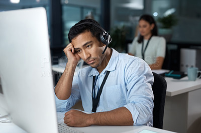 Buy stock photo Shot of a young man using a headset and looking depressed in a modern office