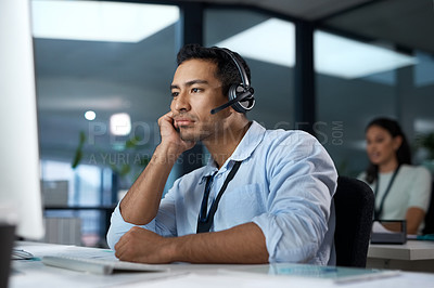 Buy stock photo Shot of a young man using a headset and looking bored in a modern office