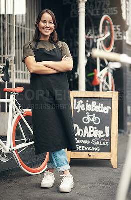 Buy stock photo Full length shot of an attractive young woman standing outside her bicycle shop with her arms folded