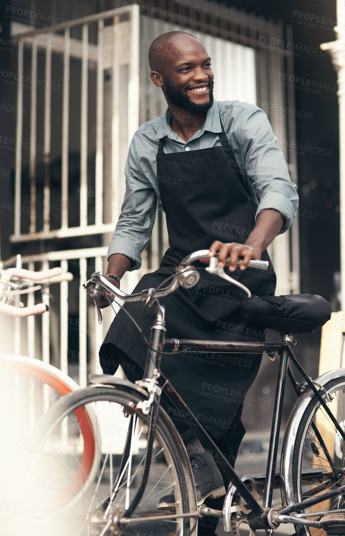 Buy stock photo Shot of a handsome young man moving a bicycle from his shop during the day