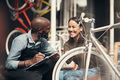Buy stock photo Shot of a handsome young man crouching outside his bicycle shop and assisting a customer