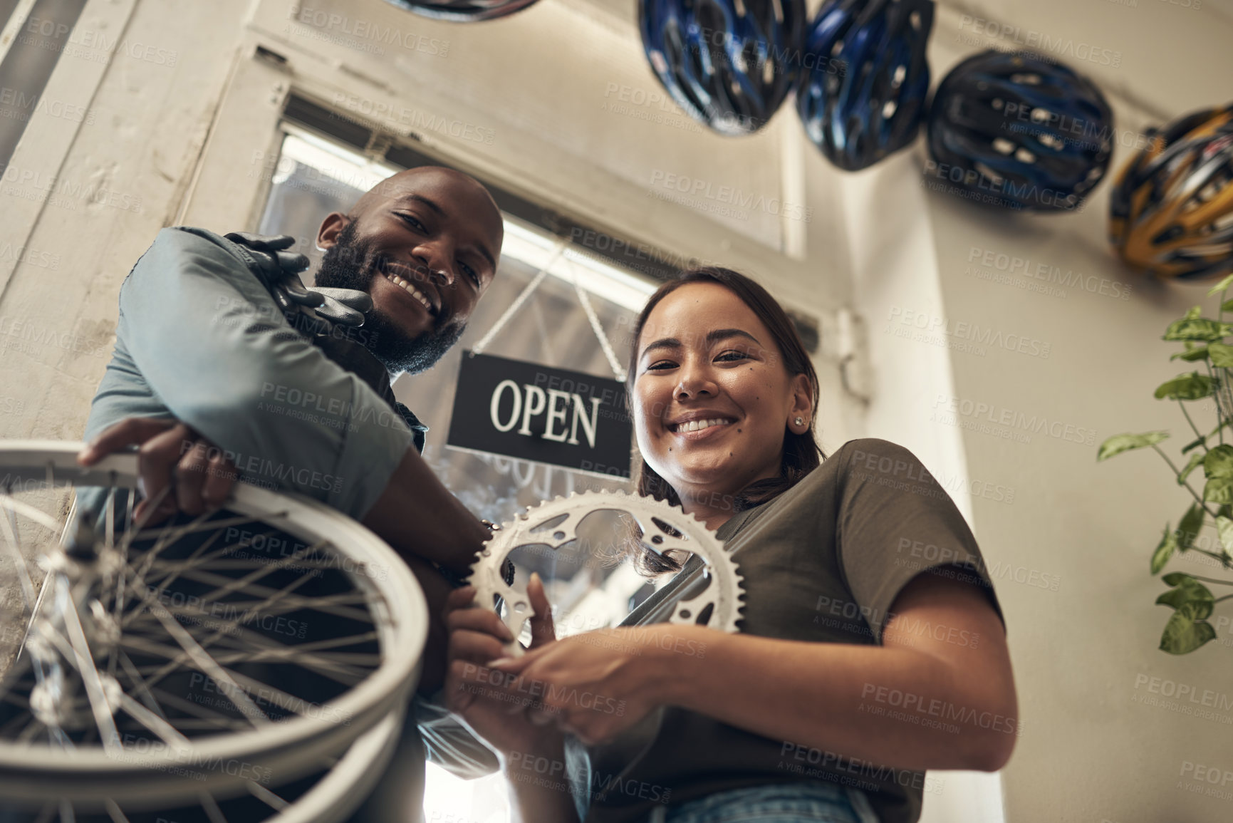 Buy stock photo Low angle shot of two young business owners standing together in their bicycle shop and holding spare parts