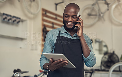 Buy stock photo Shot of a handsome young man standing alone in his bicycle shop and using technology