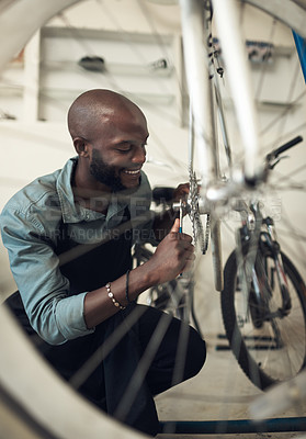 Buy stock photo Shot of a handsome young man crouching alone in his shop and repairing a bicycle wheel