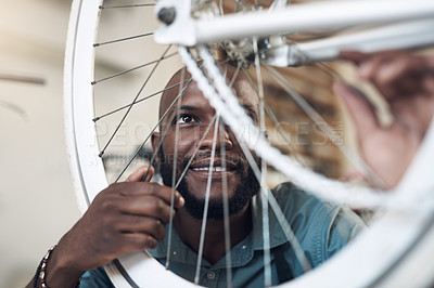 Buy stock photo Shot of a handsome young man crouching alone in his shop and repairing a bicycle wheel