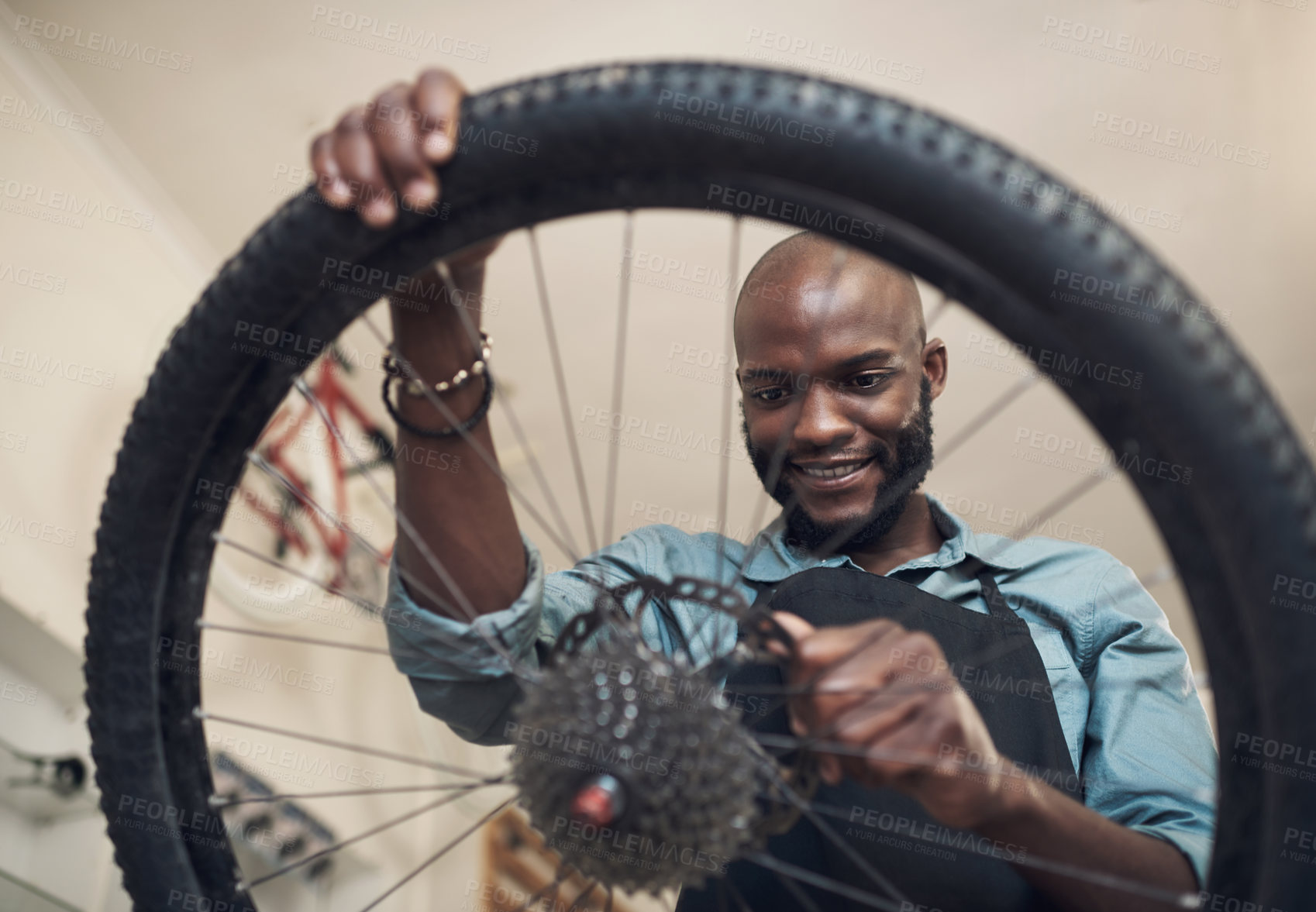 Buy stock photo Shot of a handsome young man standing alone in his shop and repairing a bicycle wheel
