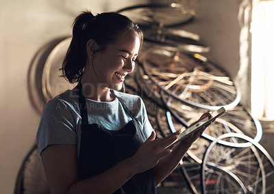 Buy stock photo Shot of a young woman using a digital tablet and working at a bicycle repair shop