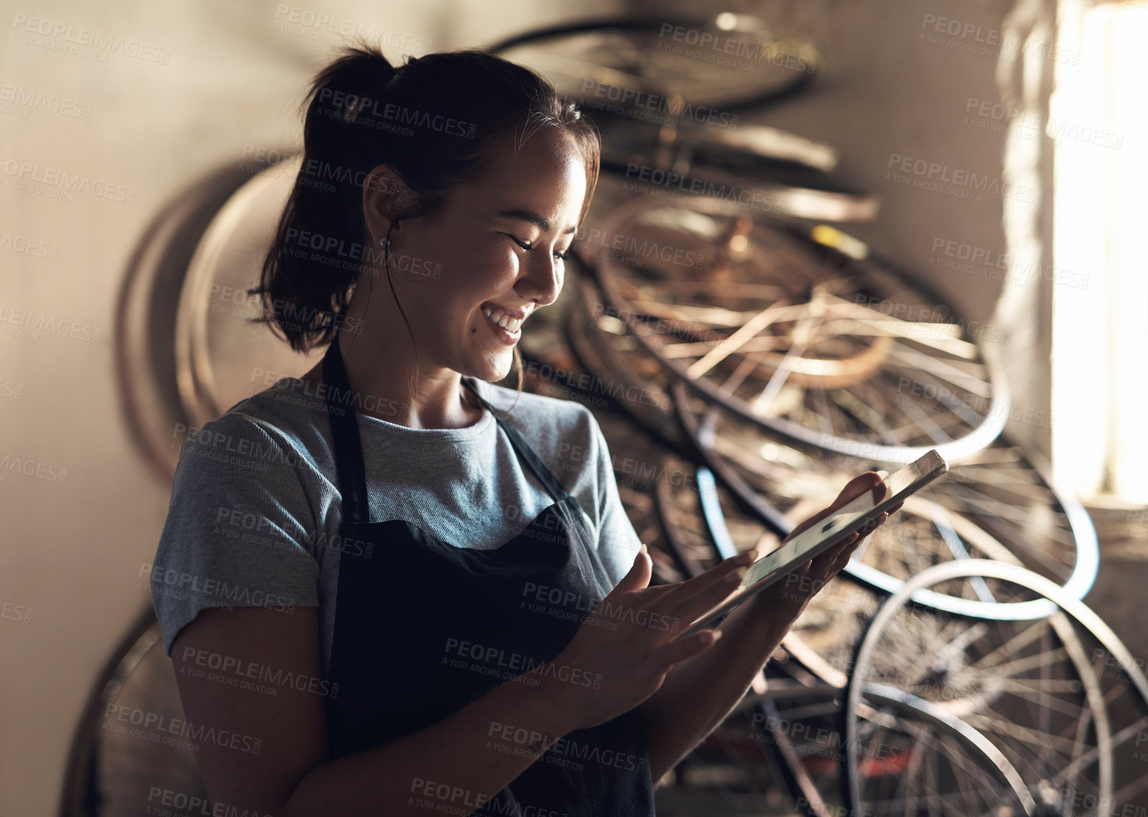 Buy stock photo Shot of a young woman using a digital tablet and working at a bicycle repair shop