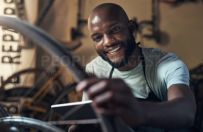 Buy stock photo Shot of a young man holding a digital tablet and working at bicycle repair shop