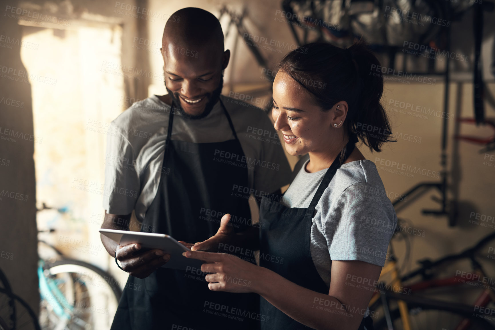 Buy stock photo Shot of two young people browsing on a digital tablet while working at a bicycle repair shop