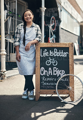 Buy stock photo Portrait of a young woman leaning on a bicycle repair shop sign outside