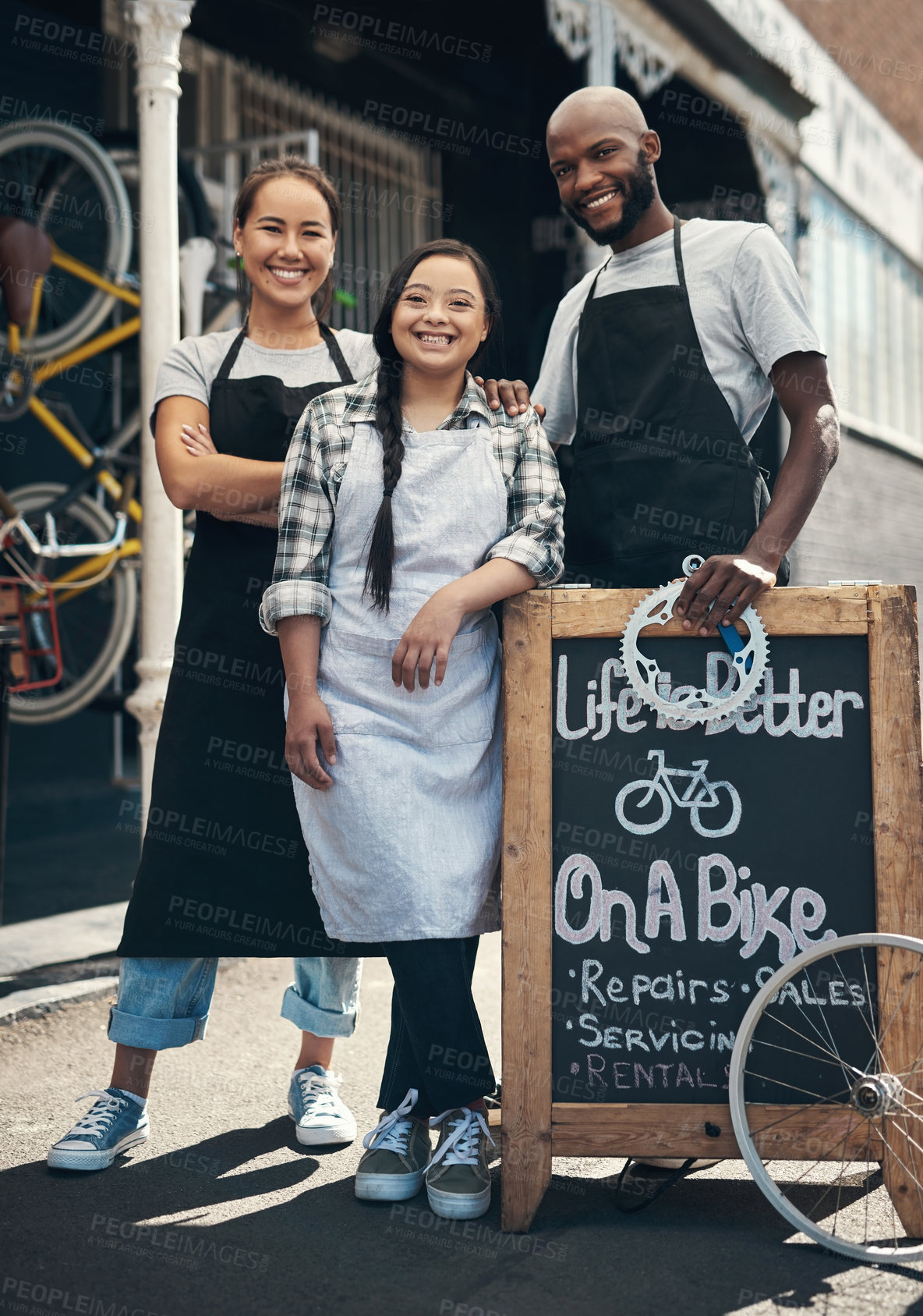 Buy stock photo Portrait of three young workers standing behind a bicycle repair sign outside