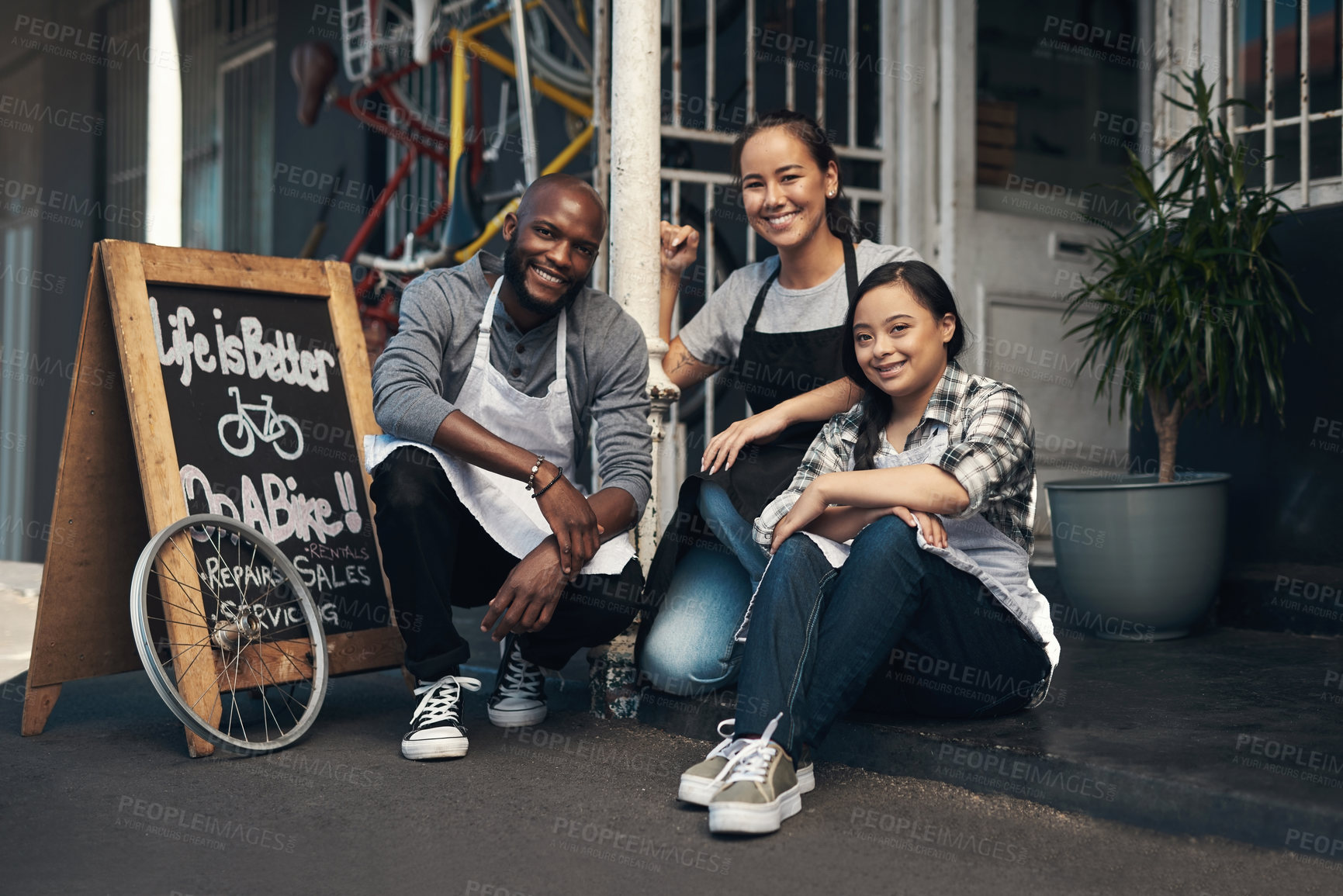 Buy stock photo Portrait of three young workers sitting outside of their bicycle repair shop