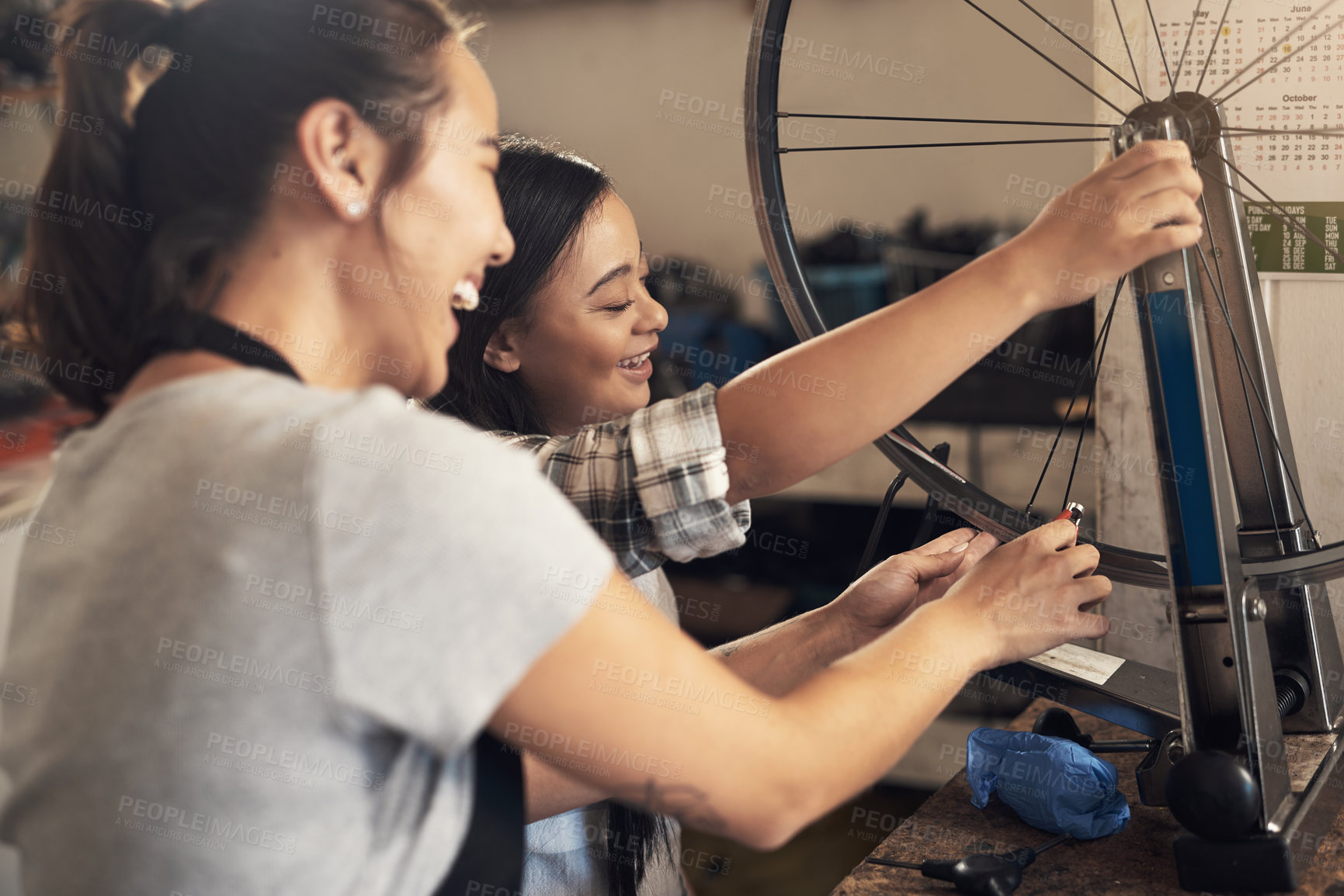 Buy stock photo Shot of two young female  workers fixing a bike at a bicycle repair shop