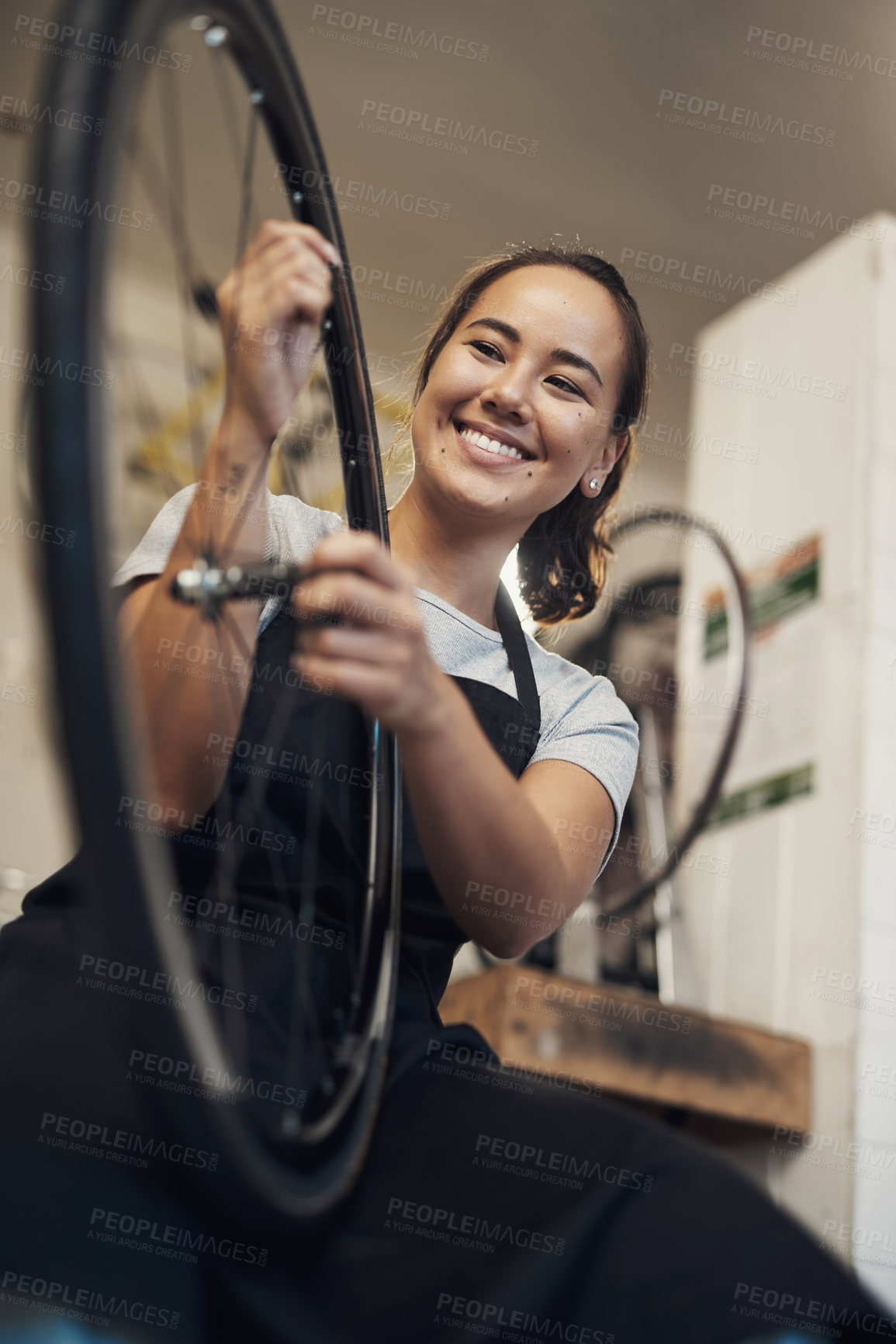 Buy stock photo Shot of an attractive young woman standing alone in her shop and repairing a bicycle wheel