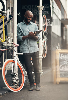Buy stock photo Full length shot of a handsome young man standing alone outside his bicycle shop and writing on a clipboard